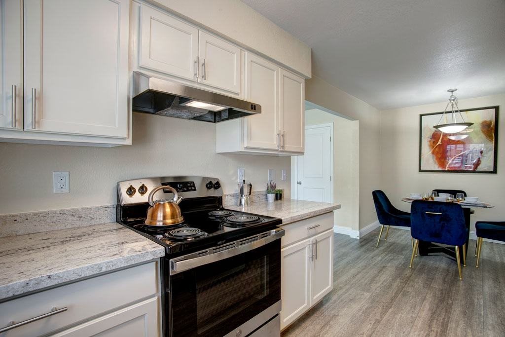 A kitchen with a stove top oven and a dining table with chairs.